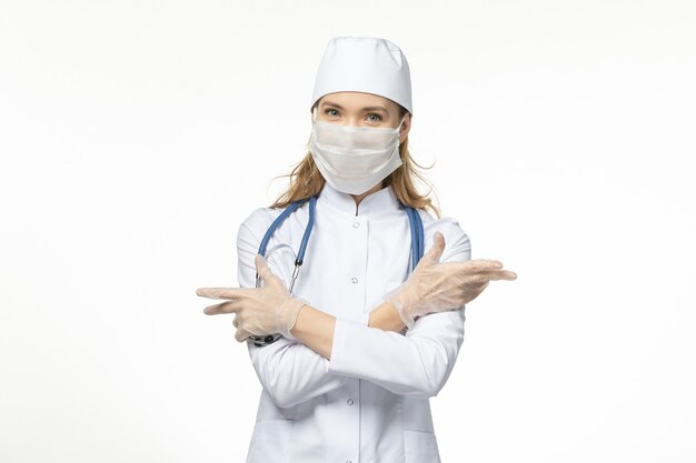 Vooraanzicht vrouwelijke arts in medisch pak masker met handschoenen dragen vanwege coronavirus op witte muur ziekte pandemisch covid-virus