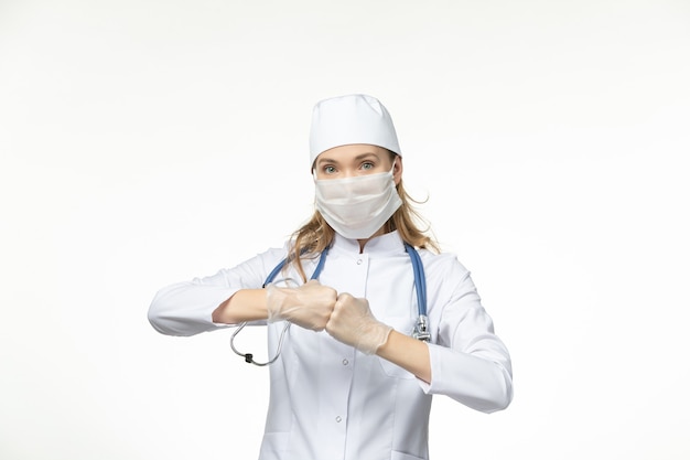 Vooraanzicht vrouwelijke arts in medisch pak met steriel masker vanwege coronavirus op witte muur pandemie gezondheidscovid-