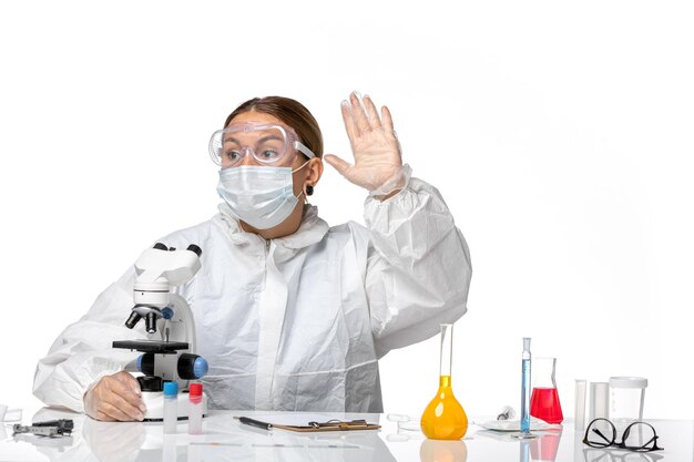 Vooraanzicht vrouwelijke arts in speciaal pak en masker met behulp van microscoop op lichte witte achtergrond covid-virus pandemisch coronavirus