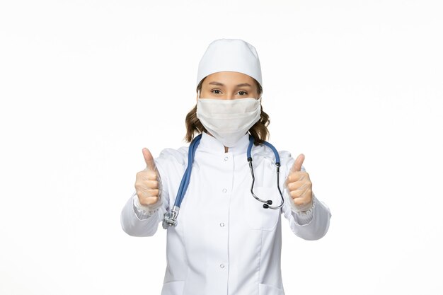 Vooraanzicht vrouwelijke arts in wit medisch pak en het dragen van masker vanwege coronavirus op het witte bureau pandemische virusziekte isolatie covid