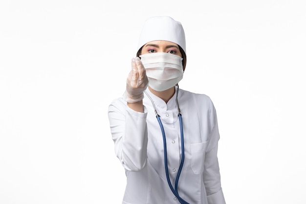 Vooraanzicht vrouwelijke arts in wit steriel medisch pak met masker vanwege coronavirus op wit bureau ziekte covid-ziektevirus