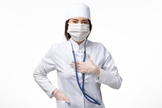Vooraanzicht vrouwelijke arts in wit steriel medisch pak met masker vanwege coronavirus op witte muur ziekte ziekte pandemie virus covid-