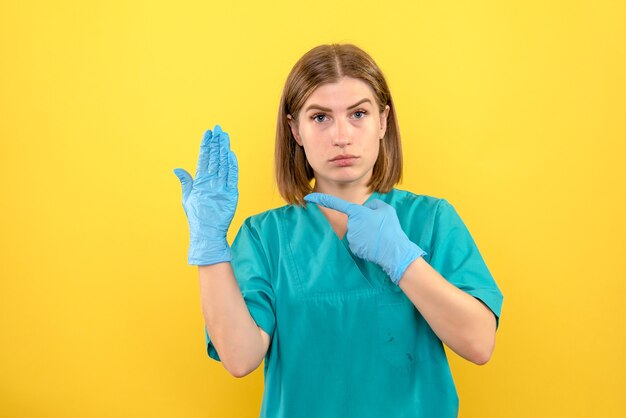 Vooraanzicht vrouwelijke arts met blauwe handschoenen op gele ruimte