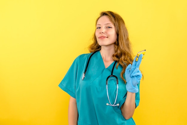 Vooraanzicht vrouwelijke arts met pillen op gele ruimte