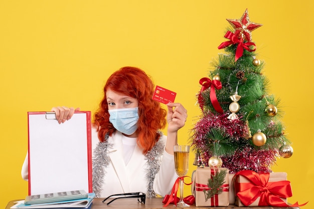 Vooraanzicht vrouwelijke arts rond kerstboom en cadeautjes zitten in masker