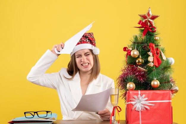 Vooraanzicht vrouwelijke artsenzitting met kerstmis stelt het houden van documenten op geel bureau voor