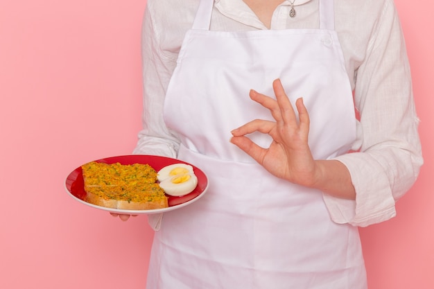 Vooraanzicht vrouwelijke banketbakker in witte slijtage met plaat met toast en ei op de roze muur kook keuken keuken eten