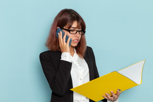 Vooraanzicht vrouwelijke beambte die geel document houdt en aan de telefoon spreekt op blauwe ondergrond