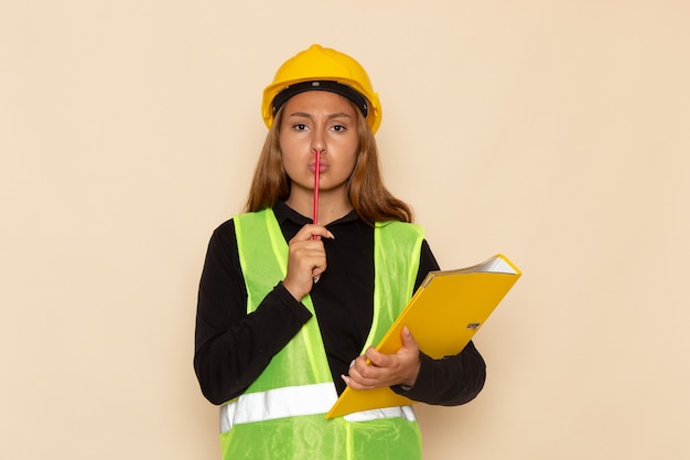 Vooraanzicht vrouwelijke bouwer die in gele helm geel dossier en potlood op de witte bouw van de bureaubouwer houdt