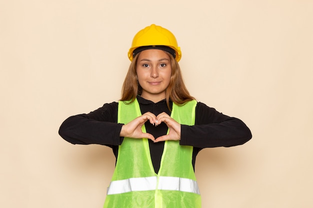 Vooraanzicht vrouwelijke bouwer in geel helm zwart shirt met hartteken op de witte muur