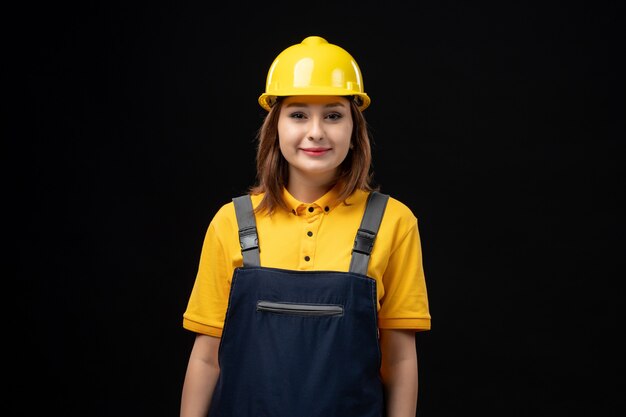 Vooraanzicht vrouwelijke bouwer in uniforme en beschermende helm op zwarte muur