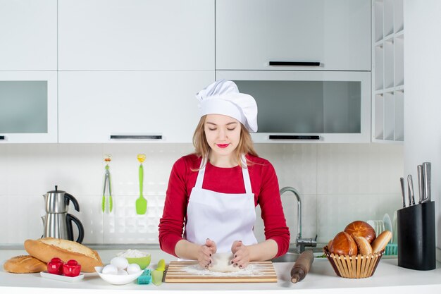 Vooraanzicht vrouwelijke chef-kok die het deeg in de keuken kneedt