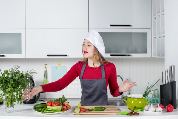 Vooraanzicht vrouwelijke chef-kok in koksmuts die hand reikt naar greens