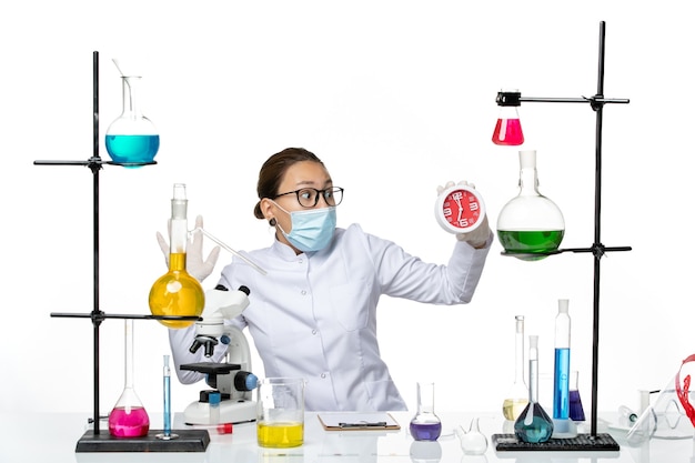 Vooraanzicht vrouwelijke chemicus in medisch pak met masker houden klokken op witte achtergrond virus lab chemie covid splash