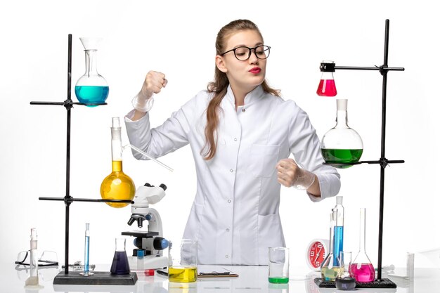 Vooraanzicht vrouwelijke chemicus in medisch pak poseren op wit bureau chemie virus pandemie covid-