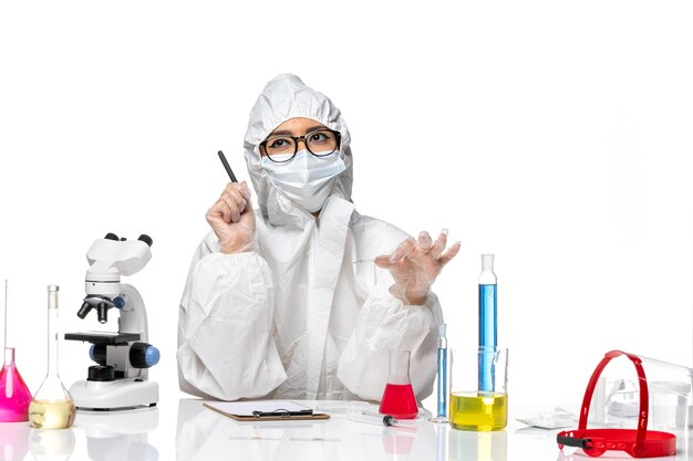 Vooraanzicht vrouwelijke chemicus in speciaal beschermend pak schrijven van notities op een witte achtergrond virus chemie covid pandemie gezondheid