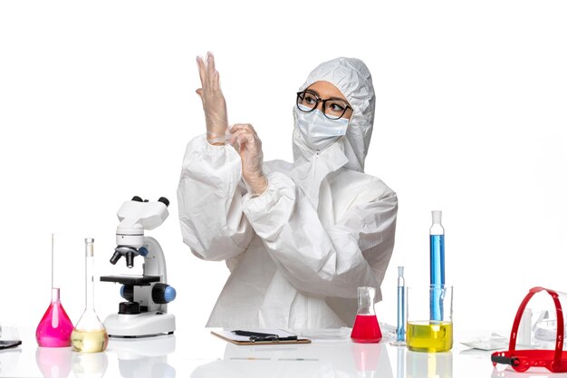 Vooraanzicht vrouwelijke chemicus in speciaal beschermend pak zitten met oplossingen die handschoenen dragen op witte achtergrond chemie pandemisch covid-virus
