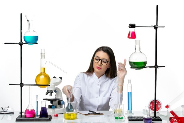 Vooraanzicht vrouwelijke chemicus in wit medisch pak bedrijf kolf met blauwe oplossing op lichte witte achtergrond lab wetenschap virus covid pandemie