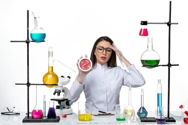 Vooraanzicht vrouwelijke chemicus in wit medisch pak met klokken op lichte witte achtergrond science virus lab covid-pandemie