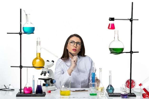Vooraanzicht vrouwelijke chemicus in wit medisch pak werken en schrijven van notities denken op witte achtergrond science virus covid-pandemic lab
