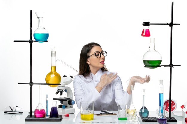 Vooraanzicht vrouwelijke chemicus in witte medische pak zittend met oplossingen op witte achtergrond science virus covid-pandemic lab