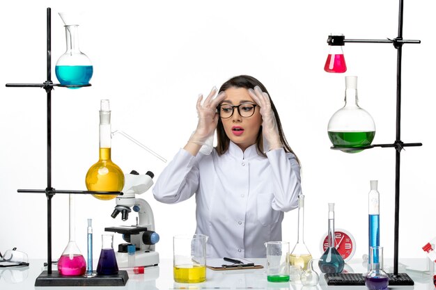 Vooraanzicht vrouwelijke chemicus in witte medische pak zittend met oplossingen op witte achtergrond wetenschap pandemie virus covid lab