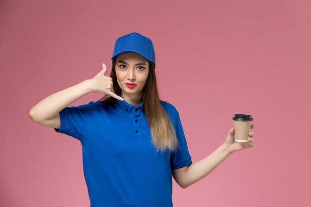 Vooraanzicht vrouwelijke koerier in blauw uniform en cape met levering koffiekopje op roze bureau baan werknemer vrouw