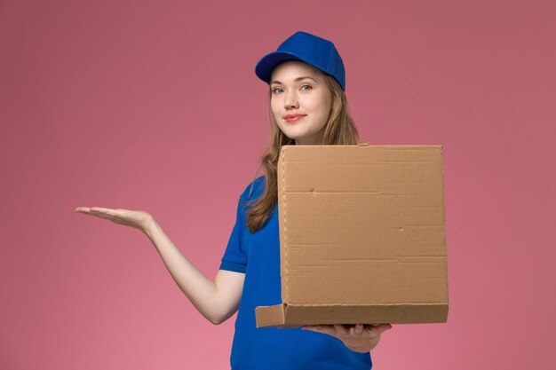 Vooraanzicht vrouwelijke koerier in blauw uniform met voedselleveringsdoos poseren met het op de roze achtergrond baan service uniform bedrijf