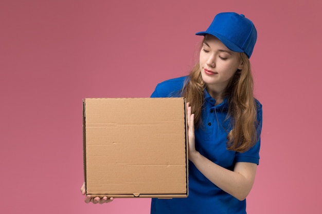 Vooraanzicht vrouwelijke koerier in blauw uniform voedselleveringsdoos houden op het roze achtergrond baan service uniform bedrijf