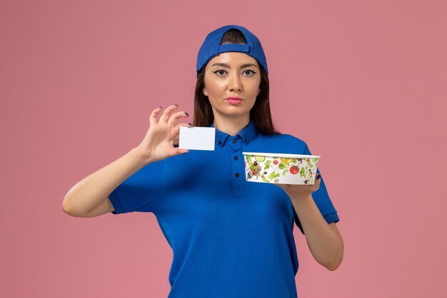 Vooraanzicht vrouwelijke koerier in blauwe uniforme cape met bezorgkom met kaart op lichtroze muur, levering van servicemedewerker