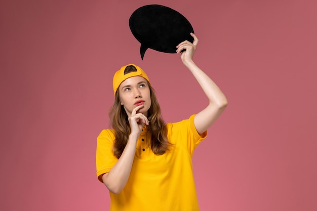 Vooraanzicht vrouwelijke koerier in geel uniform en cape met zwart bord en denken aan roze muur service levering uniform