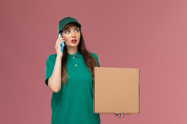 Vooraanzicht vrouwelijke koerier in groene uniforme voedseldoos met behulp van haar telefoon op roze muur dienst uniforme levering baan