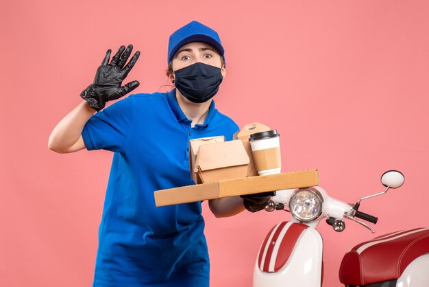 Vooraanzicht vrouwelijke koerier in masker met bezorgkoffie en eten op het roze