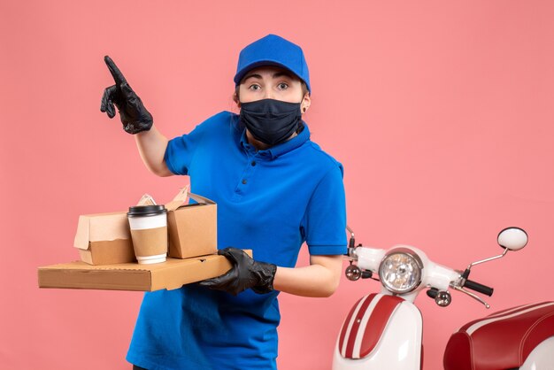 Vooraanzicht vrouwelijke koerier in masker met bezorgkoffie en eten op het roze