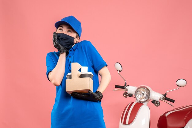 Vooraanzicht vrouwelijke koerier in masker met bezorgkoffie op het roze