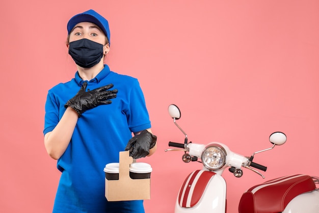 Vooraanzicht vrouwelijke koerier in masker met bezorgkoffie op lichtroze