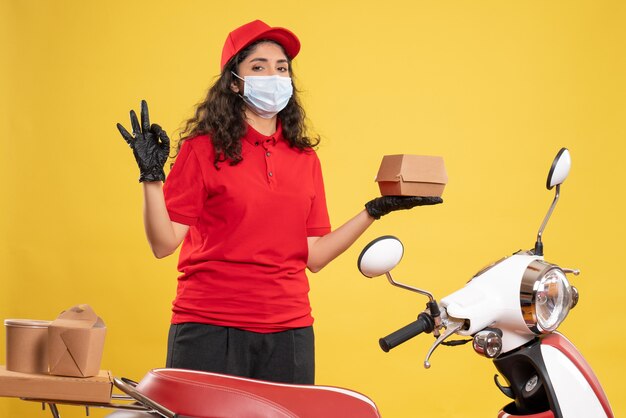 Vooraanzicht vrouwelijke koerier in rood uniform met klein voedselpakket op gele achtergrond levering covid-service uniform werknemer pandemie