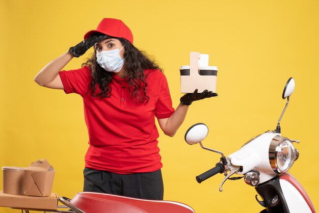 Vooraanzicht vrouwelijke koerier in rood uniform met koffiekopjes op gele achtergrond werknemer levering covid- job uniforme service