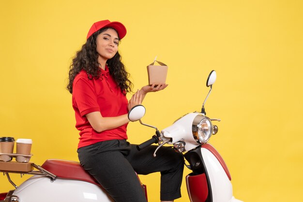 Vooraanzicht vrouwelijke koerier op de fiets voor koffie en eten bezorgen op gele achtergrond service werk levering uniforme baan vrouw