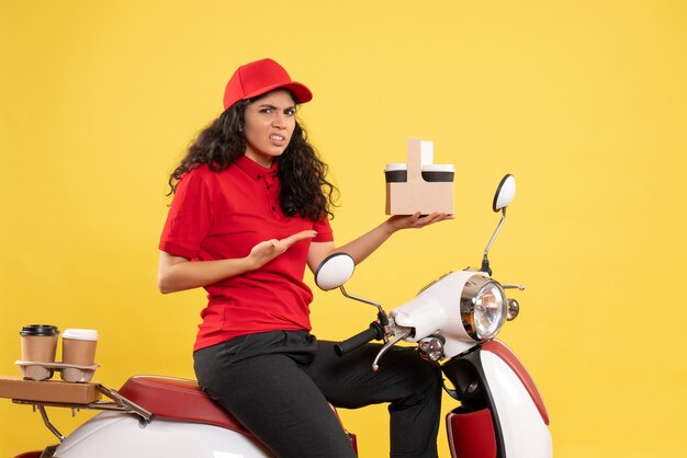 Vooraanzicht vrouwelijke koerier op de fiets voor koffiebezorging op gele achtergrond dienstverlening uniforme baan werk vrouw