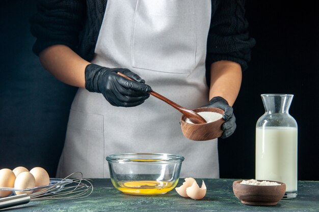 Vooraanzicht vrouwelijke kok die bloem in de eieren giet voor deeg op donkere gebak taart taart bakkerij werknemer hotcake keuken baan