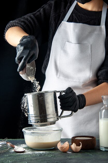 Vooraanzicht vrouwelijke kok die bloem in eieren giet op de donkere hotcake gebak taart taart keuken baan deeg werknemer