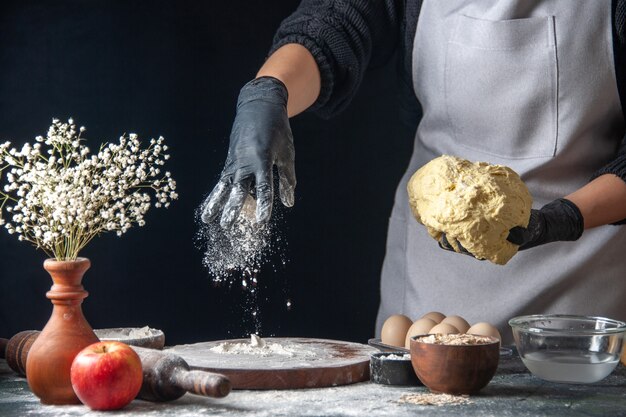 Vooraanzicht vrouwelijke kok die deeg uitrolt met bloem op de donkere baan deeg gebak keuken hotcake keuken bakkerij ei