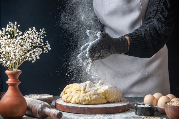 Vooraanzicht vrouwelijke kok die deeg uitrolt met bloem op de donkere baan rauw deeg bakkerij taart oven gebak hotcake