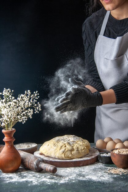Vooraanzicht vrouwelijke kok die deeg uitrolt met bloem op donkere baan deeg bakkerij taart oven gebak hotcake