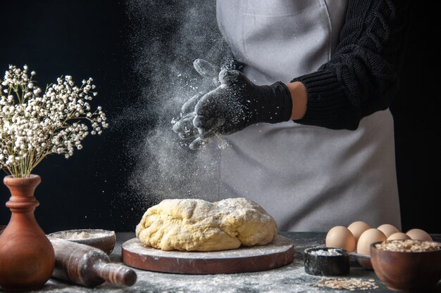 Vooraanzicht vrouwelijke kok die deeg uitrolt met bloem op donkere baan rauw deeg hotcake bakkerij taartoven