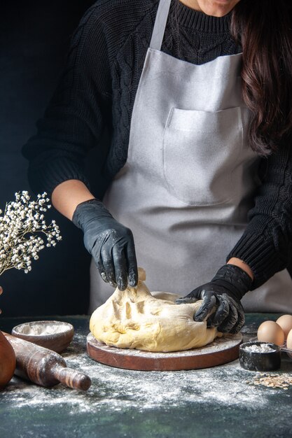 Vooraanzicht vrouwelijke kok die deeg uitrolt op de donkere banketbaan rauw deeg hotcake bakkerij taartoven