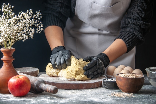 Vooraanzicht vrouwelijke kok die deeg uitrolt op donkere keuken baan gebak hotcake ei keukendeeg