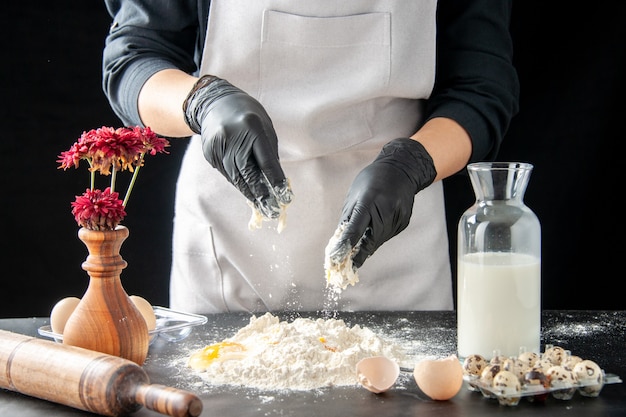 Vooraanzicht vrouwelijke kok die eieren in meel breekt op donkere baan gebak taart bakkerij koken cake biscuit deeg bakken