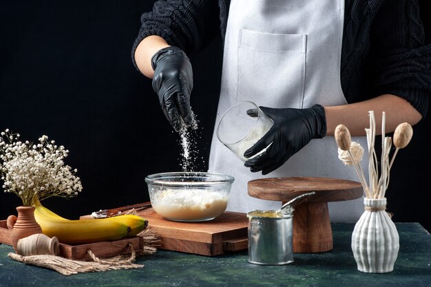 Vooraanzicht vrouwelijke kok die kokospoeder op gecondenseerde melk giet op donkere achtergrond